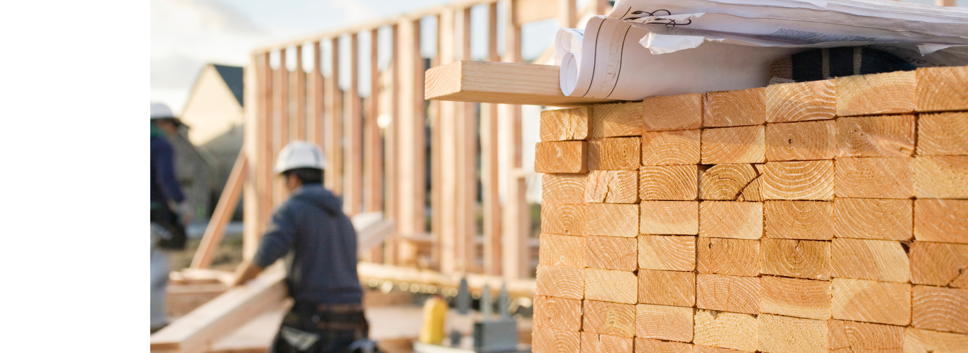 Pile of lumber stacked in the foreground in a photo of a construction site